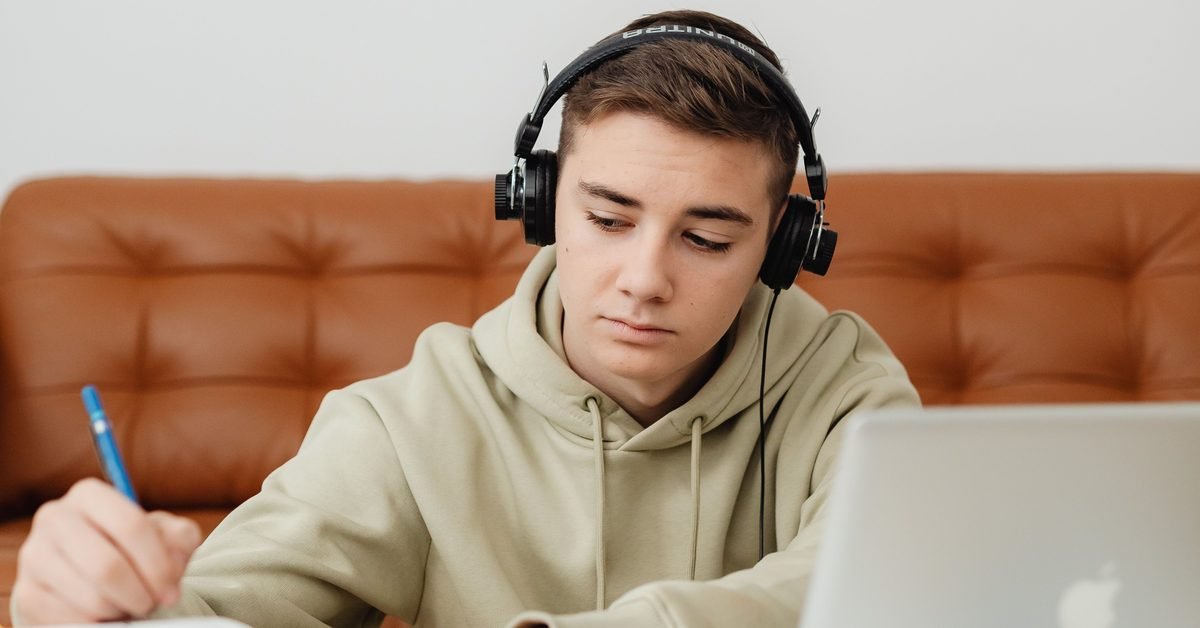 A recent matriculant wearing headphones, studying at a laptop with notes at home